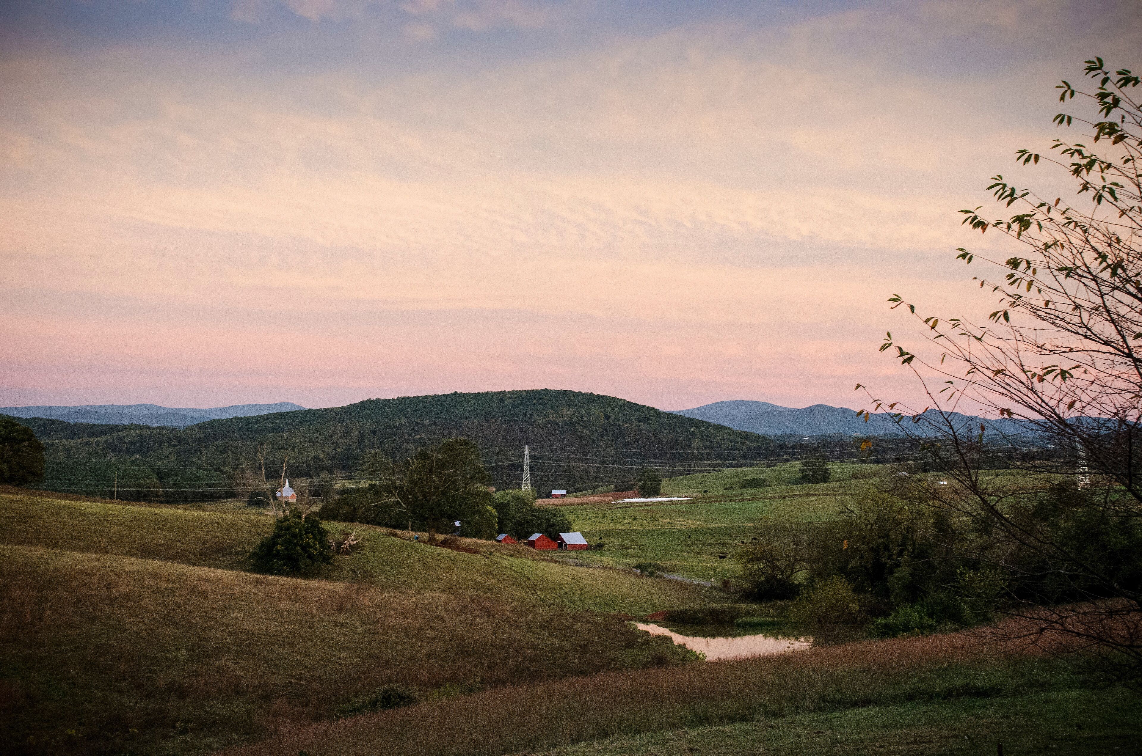 A rural landscape with rolling hills, a small house, and a power line tower.