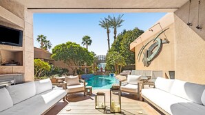 A poolside area with white sofas, a table with candles, and a TV screen. - SWIM UP POOL BAR/SPA, POOL TABLE,6 EN SUITES, PING PONG, PUTTING GREEN 227370 (La Quinta)