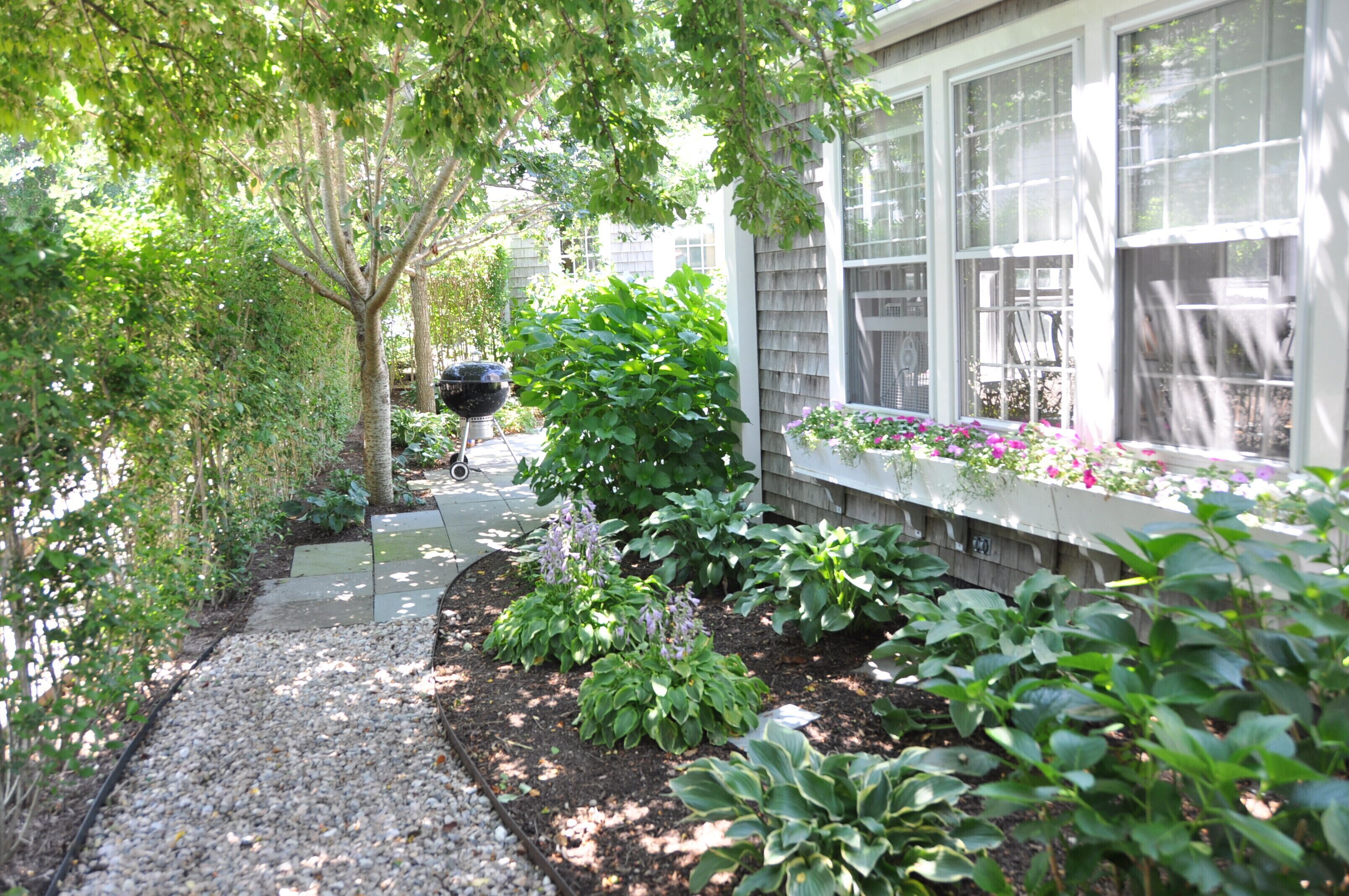 A garden pathway leading to a house with a window box of flowers.