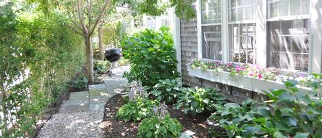 A garden pathway leading to a house with a window box of flowers.