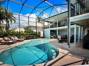 A pool area with a glass enclosure, lounge chairs, and a covered patio with outdoor furniture.