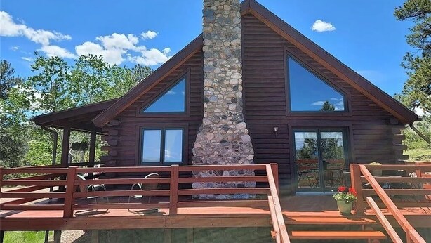 Eine Blockhütte mit einem Steinsschornstein, großen Fenstern und einer Holzdiele.