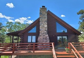 A log cabin with a stone chimney, large windows, and a wooden deck. - Spacious Log Cabin with Expansive Mountain Vistas, National Forest (Guffey)