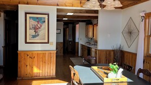 Ein geräumiger Essbereich mit hoher Decke und Holzbalken, ausgestattet mit einem großen Tisch und Stühlen, einer hängenden Leuchte und einem gerahmten Bild an der Wand.