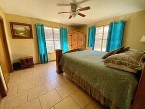 A bedroom with a bed, a ceiling fan, a wooden wardrobe, and a window with curtains.