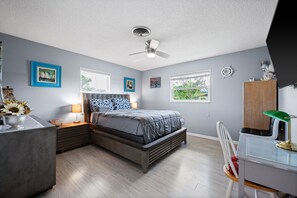 Ein Schlafzimmer mit Bett, Nachttischen, Schreibtisch, Stuhl, Deckenventilator und Fenster.