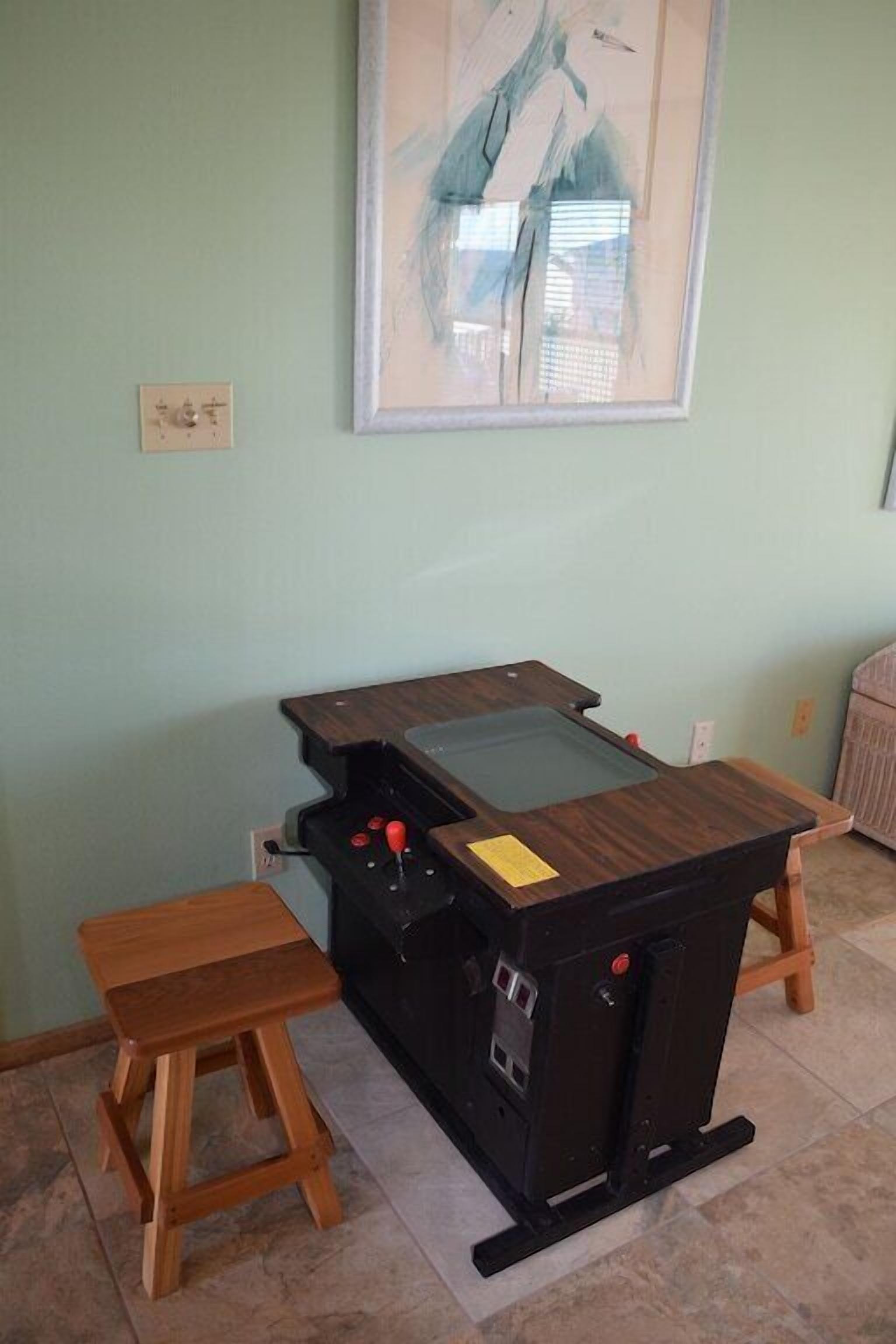 A room with a wooden table and a small stool, a framed abstract painting on the wall, and a light switch.