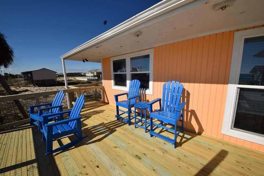 A wooden deck with blue Adirondack chairs, a covered porch, and a building with orange siding and white trim.