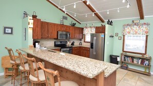 A kitchen with wooden cabinets, a granite countertop, a stainless steel refrigerator, and a bar area with chairs. - Summer Sale! Steps to Beach, Amazing View! Pool, Game room, Hot-tub! (St George Island)