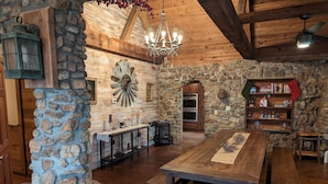Un intérieur rustique avec un mur en pierre, des poutres en bois, un lustre, une table en bois et une bibliothèque.