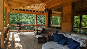 Un espace extérieur abrité, doté d'une terrasse en bois, de meubles en osier et d'un canapé moelleux avec des coussins bleus.