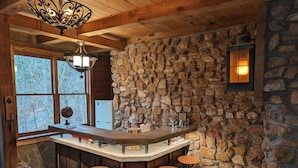 Une cuisine rustique avec un mur en pierre, un plafond en bois et un coin bar avec des tabourets.