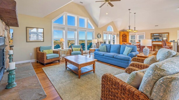 A spacious living room with a large blue sofa, wicker furniture, and a fireplace. - Premier Oceanfront Dog Friendly Home w/ Pool, Hot Tub, EV Charger, and Game Room (Salvo)