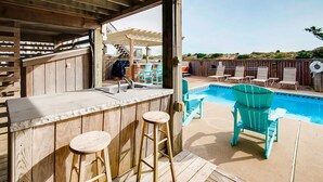 An outdoor bar area with a pool, wooden deck, and outdoor seating. - Premier Oceanfront Dog Friendly Home w/ Pool, Hot Tub, EV Charger, and Game Room (Salvo)
