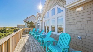 A wooden deck with turquoise Adirondack chairs, a wooden railing, and a view of the ocean. - Premier Oceanfront Dog Friendly Home w/ Pool, Hot Tub, EV Charger, and Game Room (Salvo)