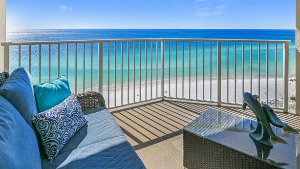 Ein Balkon mit Blick auf einen Strand, ein Sofa mit gemusterten Kissen und eine dekorative Skulptur.