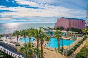 Un resort con una gran piscina, palmeras y vista al océano.