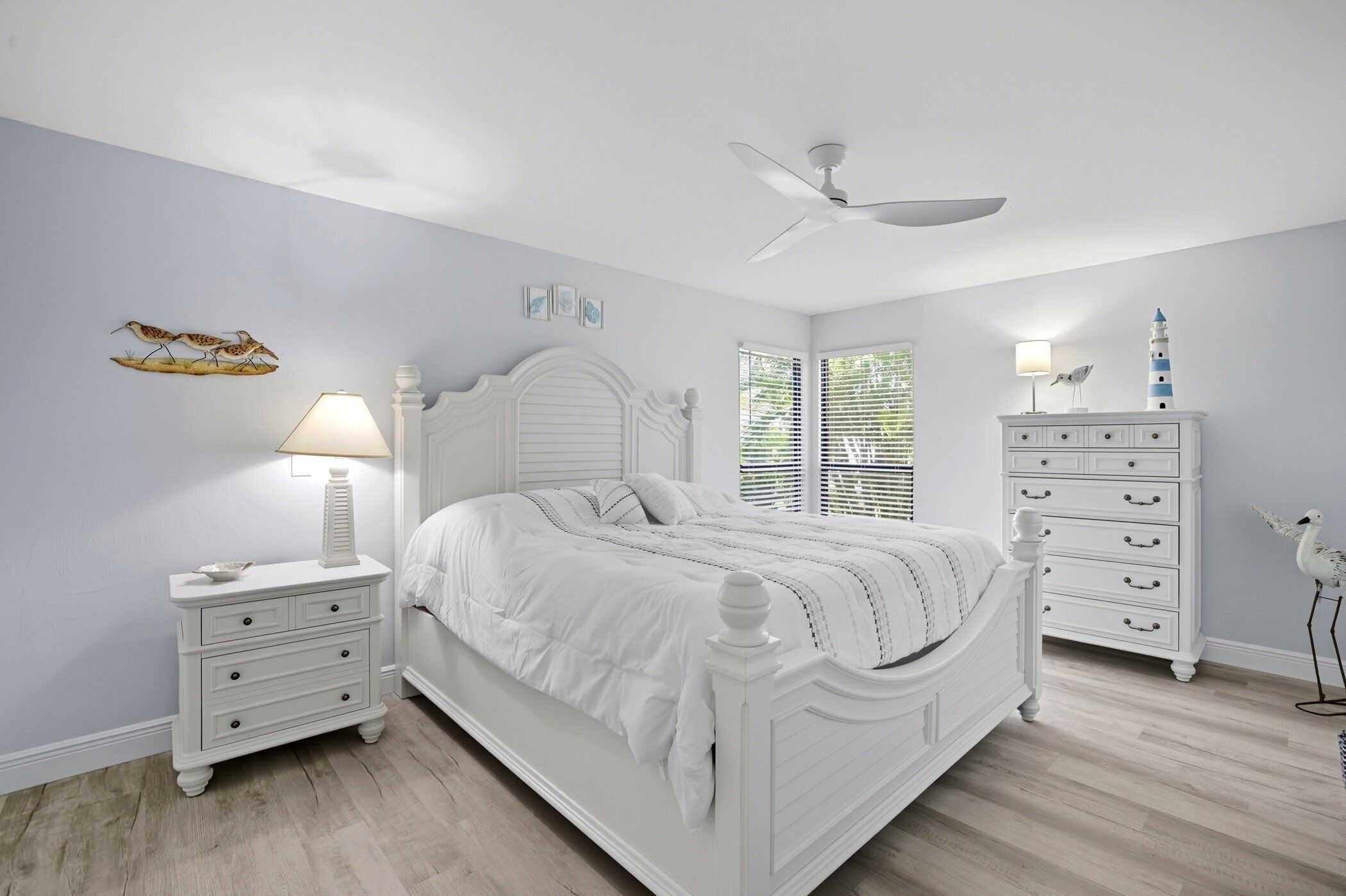 A bedroom with a white bed, nightstands, a dresser, and a ceiling fan.