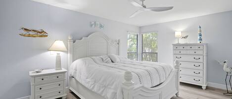 A bedroom with a white bed, nightstands, a dresser, and a ceiling fan.