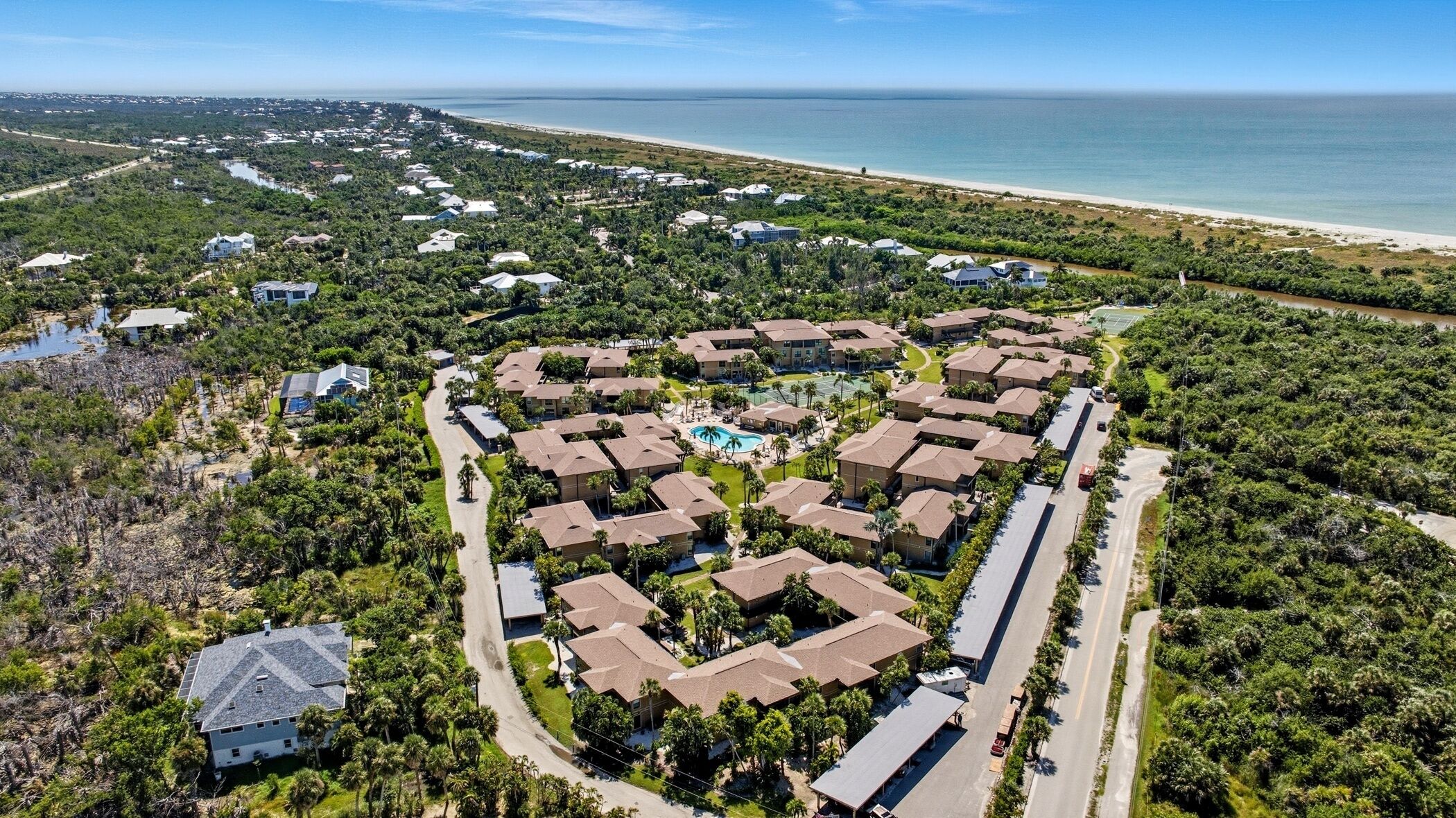 Vista aérea de un complejo turístico con una piscina central, rodeado de edificios residenciales, una playa y un río.