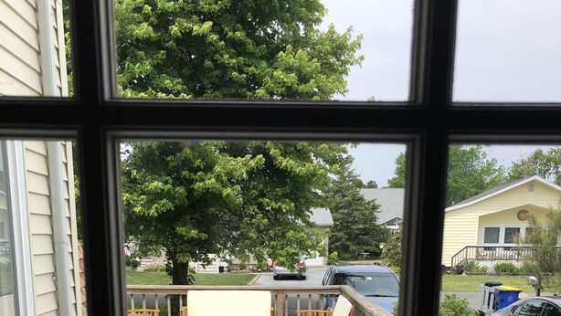 Une terrasse dotée de meubles en bois et d’un espace barbecue couvert, offrant une vue sur un quartier résidentiel.
