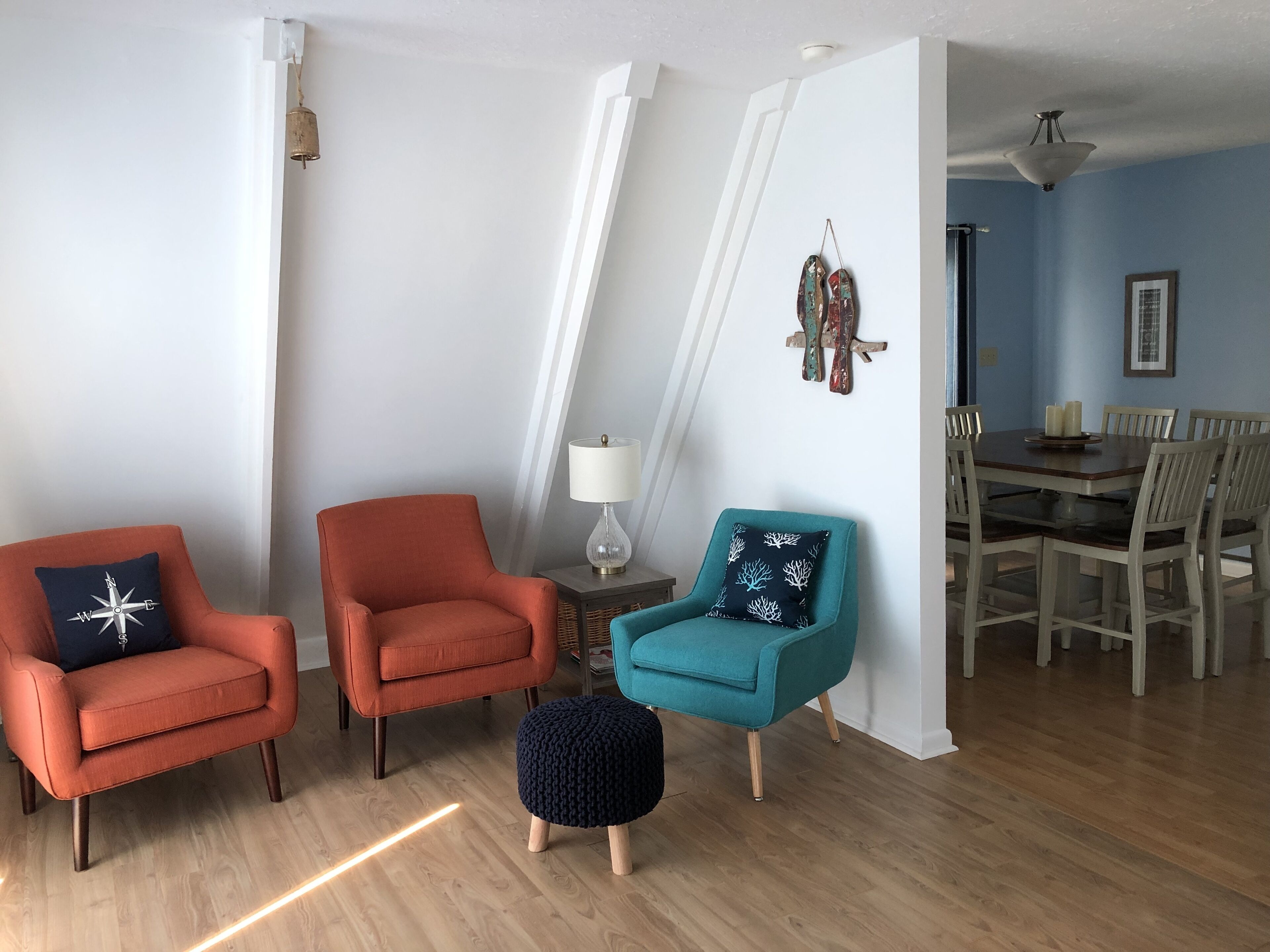 Una sala de estar con dos sillones naranjas, un sillón verde azulado, un pequeño otomaní y un comedor con mesa y sillas.
