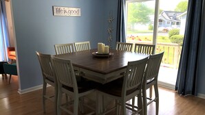 Un coin repas avec une table en bois et des chaises blanches, un centre de table composé de bougies et un panneau décoratif au mur.