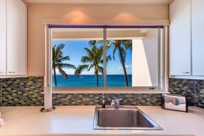 Cozinha com vista para palmeiras e o oceano, pia moderna e painel de azulejos.