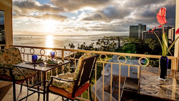 A balcony with a view of the ocean and city skyline, featuring a table with chairs and a vase of flowers. - Beach Front Studio With Spectacular Ocean Views (Honolulu)