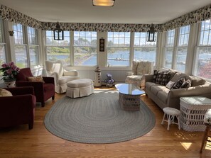 A cozy living room with a large window overlooking a lake, furnished with a sofa, chairs, and a coffee table.