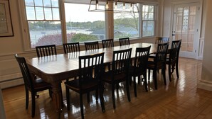 Una sala da pranzo con un grande tavolo in legno e sedie, ampie finestre con vista su un porto turistico e alberi, e un lampadario.