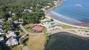 Vista aerea di una zona residenziale costiera con case, una spiaggia e un campo da tennis.