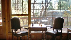 Une pièce avec deux chaises et une table, de grandes fenêtres donnant sur des arbres et une terrasse à l’extérieur.