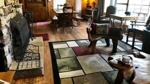L’intérieur d’un chalet chaleureux, avec une cheminée en pierre, des meubles en bois et une grande fenêtre.