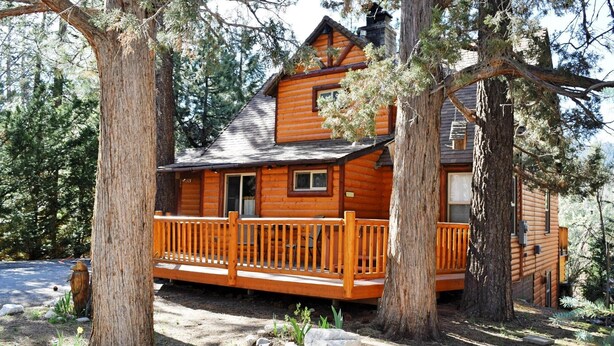 Une cabane en rondins avec une terrasse en bois, entourée d’arbres et de rochers.