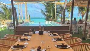 An outdoor dining area with a view of the ocean, tables set with plates and cutlery, and chairs arranged around the tables. - 5 Star Rated, Beautiful Beach Best Value at Bavaro Beach! No Extra Fees (Punta Cana)