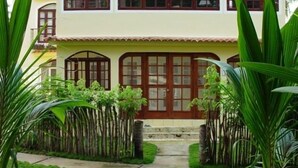 A two-story building with a yellow facade and a red door. There are multiple windows with brown frames, and the building is surrounded by lush greenery. - 5 Star Rated, Beautiful Beach Best Value at Bavaro Beach! No Extra Fees (Punta Cana)