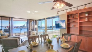 Ein Essbereich mit Blick auf den Strand, einem Deckenventilator und einem an der Wand montierten Fernseher.