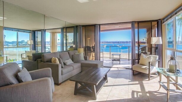 Ein modernes Wohnzimmer mit einer großen Couch, einem Couchtisch und Meerblick durch raumhohe Fenster.