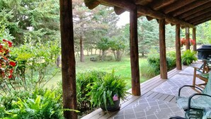 Un porche cubierto con vigas de madera, un jardín con césped y plantas en macetas.