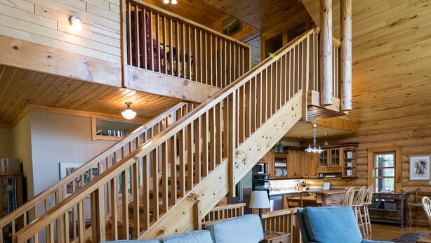 Amplia sala de estar con una escalera de madera, un sofá, una silla y una cocina al fondo.