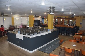 A buffet area with a central serving station, bar stools, and wooden tables with chairs.