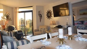 Habitación de hotel con balcón, sofá, mesa de comedor con velas y televisor montado en la pared.