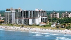 Un hotel frente a la playa con varios edificios altos, una playa de arena y vistas al océano.