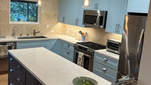 A modern kitchen with light blue cabinets, a stainless steel refrigerator, a microwave, and a large island with a bowl of fruit. - Vineyard FarmStay, & Heated Pool from May-Oct. (Glen Ellen)