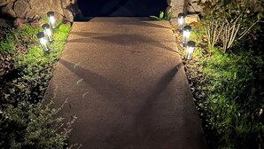 A pathway flanked by stone walls and illuminated by ground lights, leading into a dark area. - Vineyard FarmStay, & Heated Pool from May-Oct. (Glen Ellen)