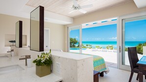 A modern bathroom with a large mirror, a sink, and a plant. It leads to a balcony with a view of the ocean. - Villa Blue Heaven-Just Steps to  Beach and Turquoise Water -  Best Sunsets!  (Providenciales)