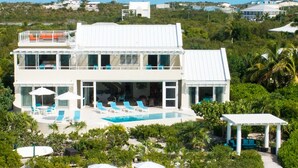 A large, two-story beachfront property with a swimming pool, multiple lounge chairs, and a covered patio area. - Villa Blue Heaven-Just Steps to  Beach and Turquoise Water -  Best Sunsets!  (Providenciales)