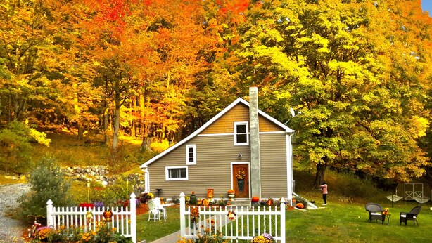 A two-story house with a white picket fence, surrounded by autumn foliage.