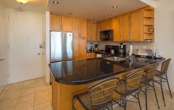 A modern kitchen with wooden cabinets, a stainless steel refrigerator, a microwave, and a large island with bar stools.